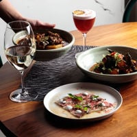 On this wooden Golden Boy table, you'll spot a white wine, cocktail, sashimi and massman curry.