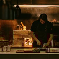 Chef slices a leak at Restaurant Botanic with flames of the open fire oven roaring behind him.